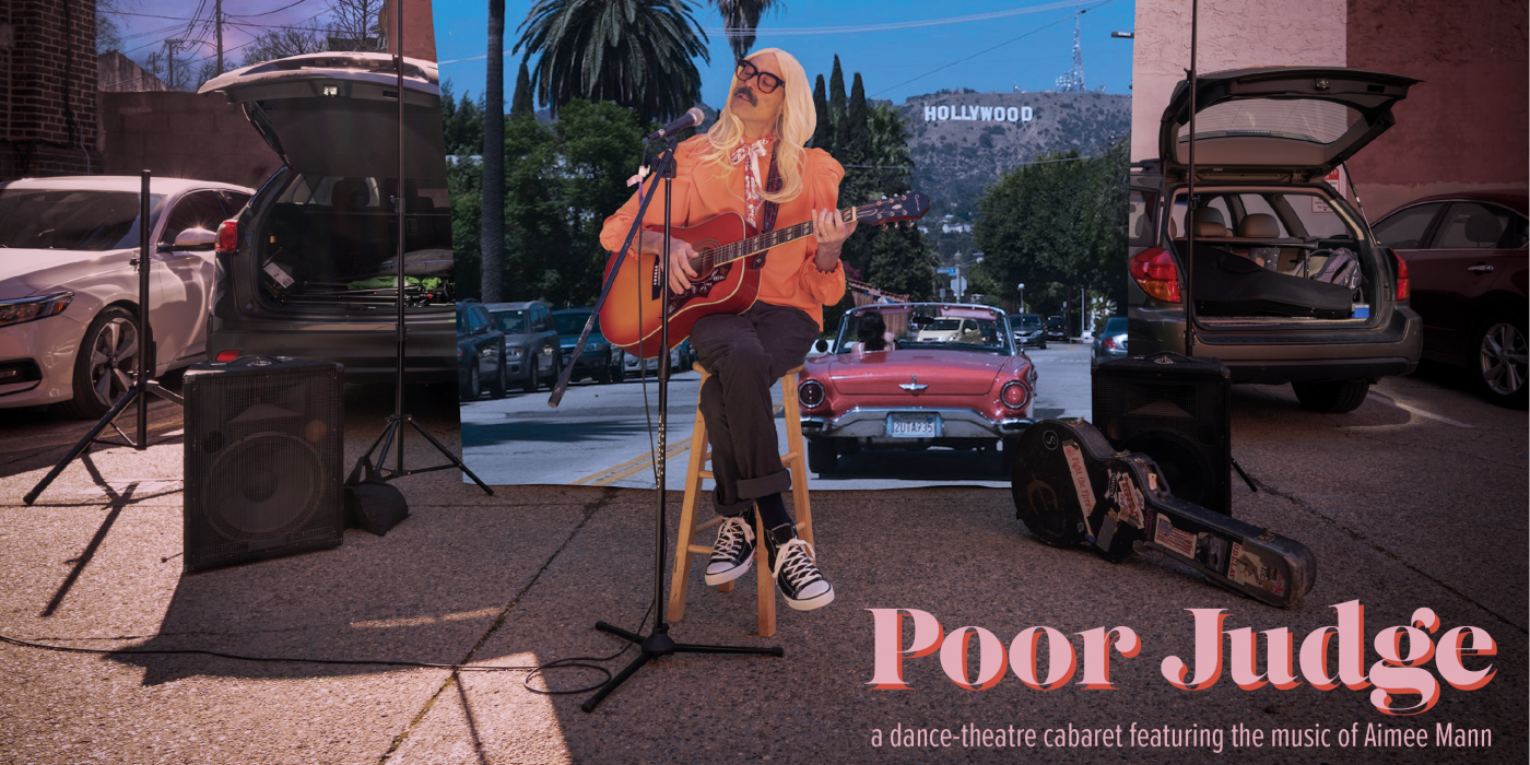 Dito dressed as Aimee Mann sits in a parking lot with an image of LA behind him