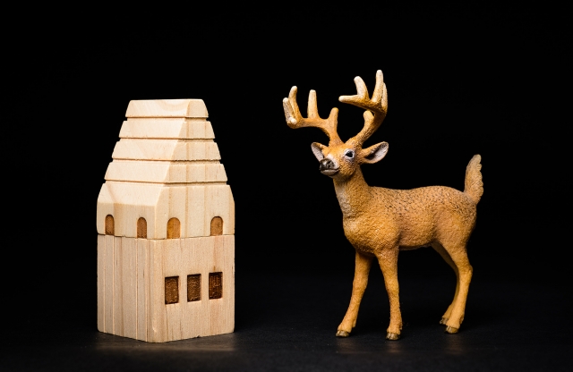 A photograph of a toy deer and a wooden toy house.